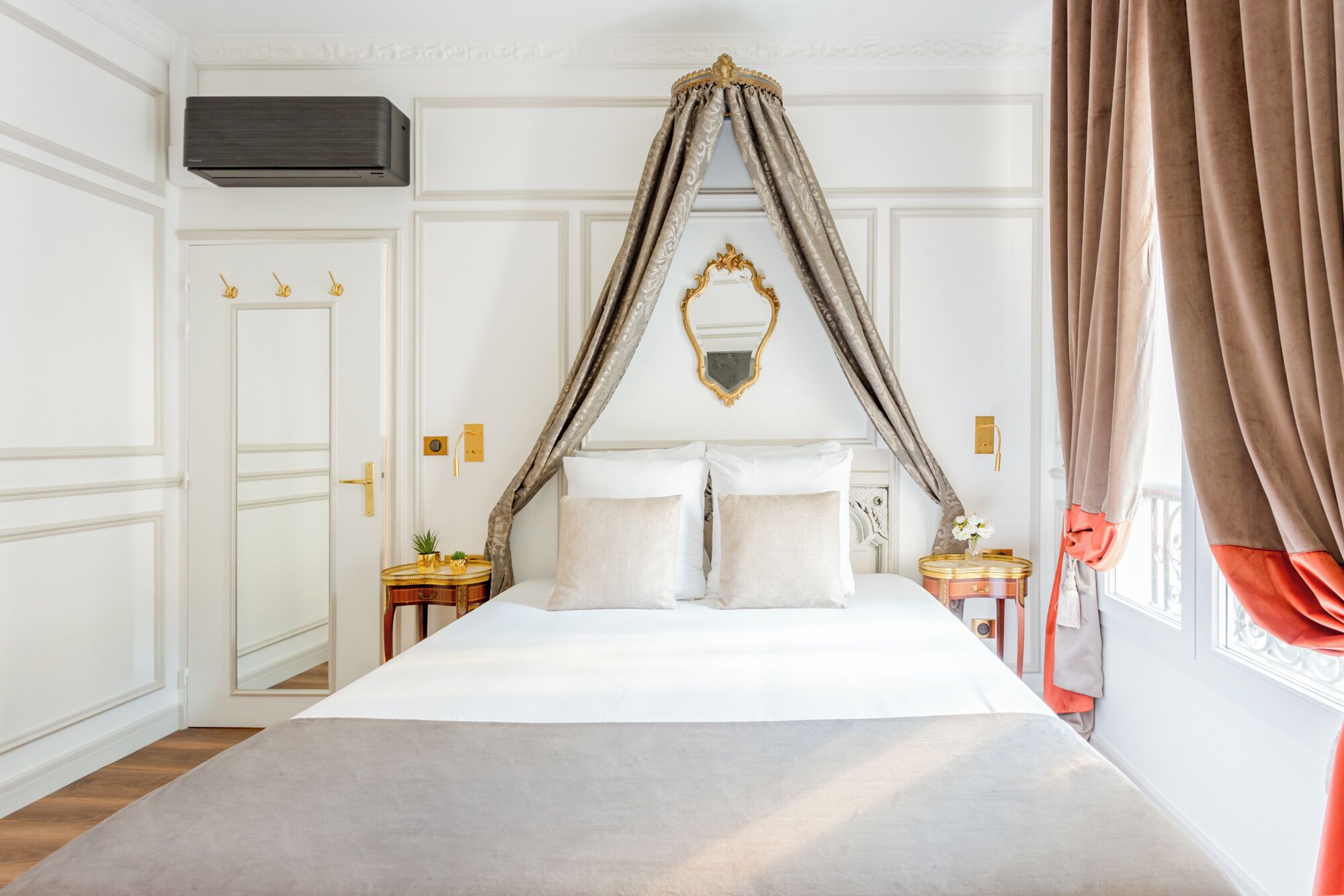 A bedroom with a canopy bed, a wardrobe, a bedside table with a lamp, and a window with curtains.