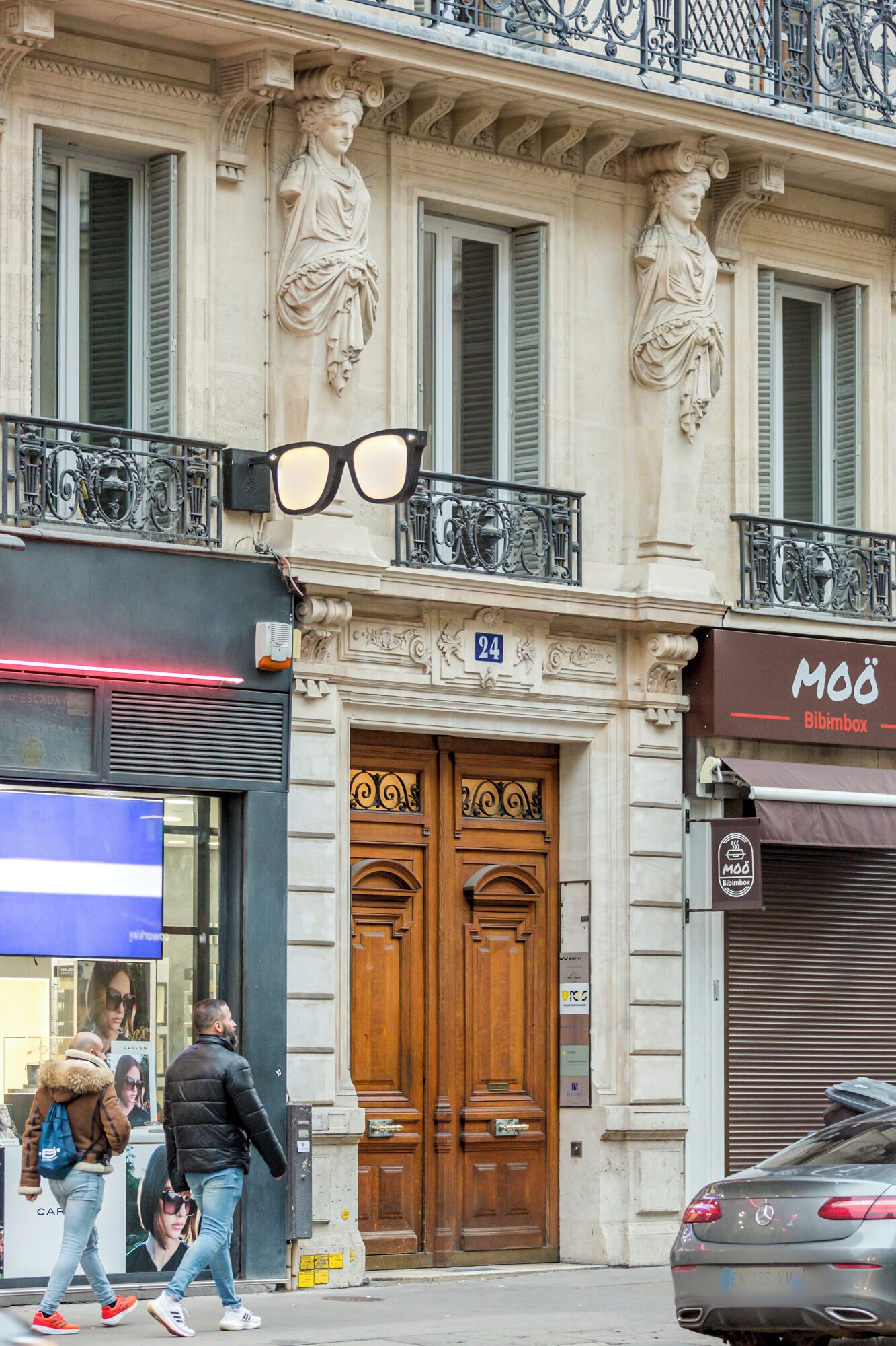 A building with classical architecture, featuring ornate sculptures, a double door entrance, and a balcony with decorative railings.