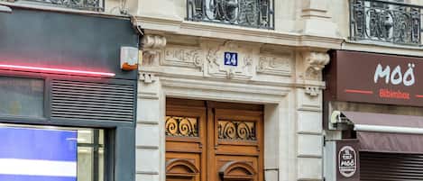 A building with classical architecture, featuring ornate sculptures, a double door entrance, and a balcony with decorative railings.