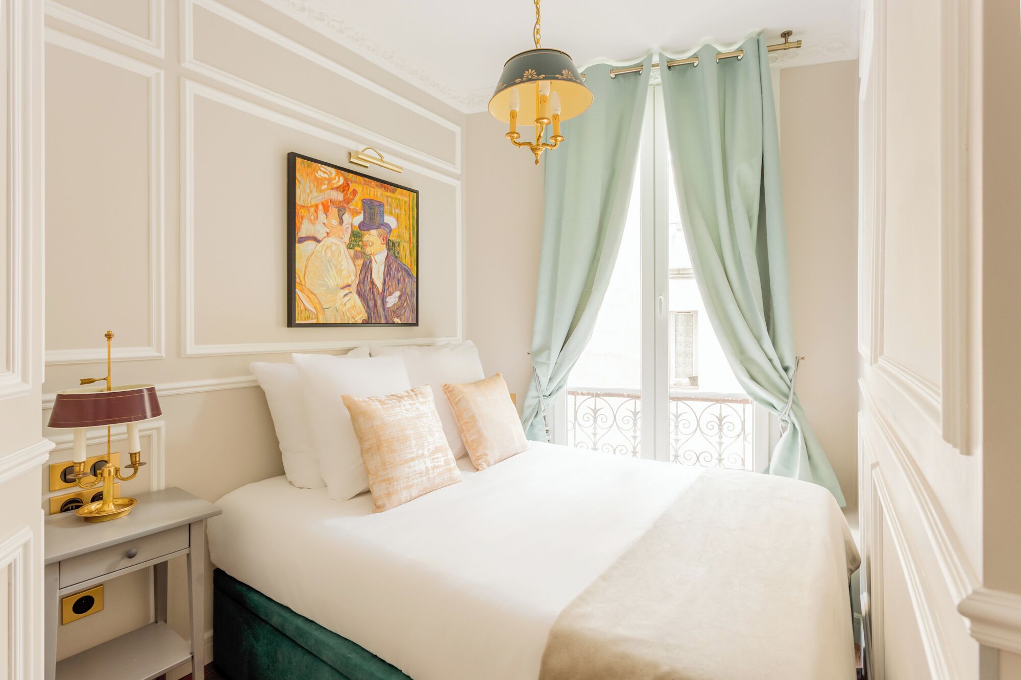 Ein Hotelzimmer mit Bett, Nachttisch, Lampe, einem Gemälde und einem Balkon mit Vorhängen.