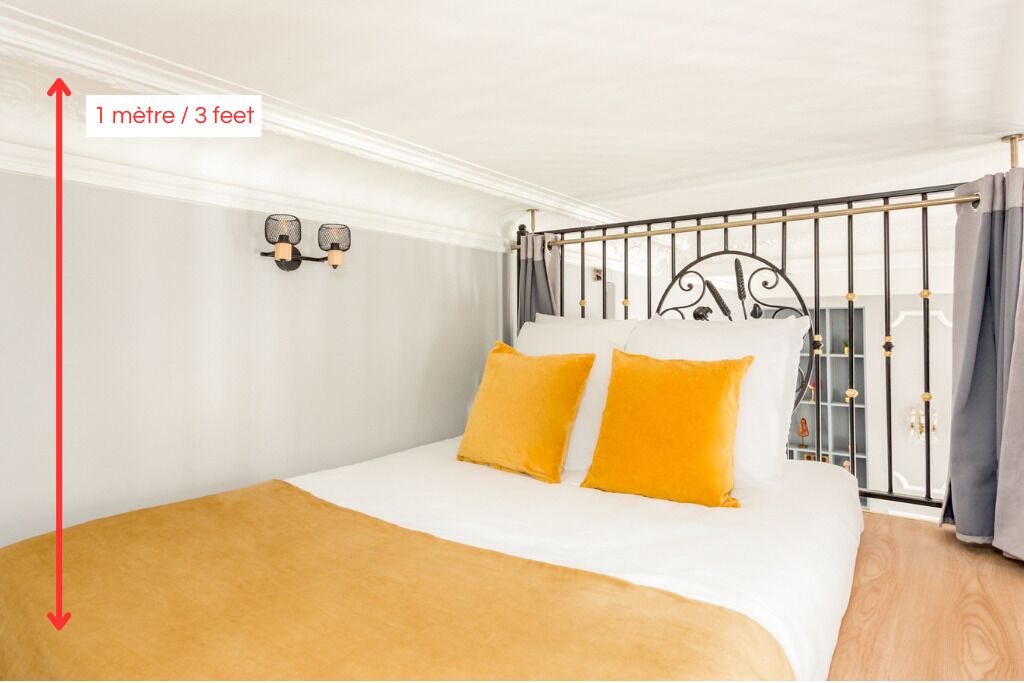 A bedroom with a bed, two wall-mounted lamps, and a window with curtains.