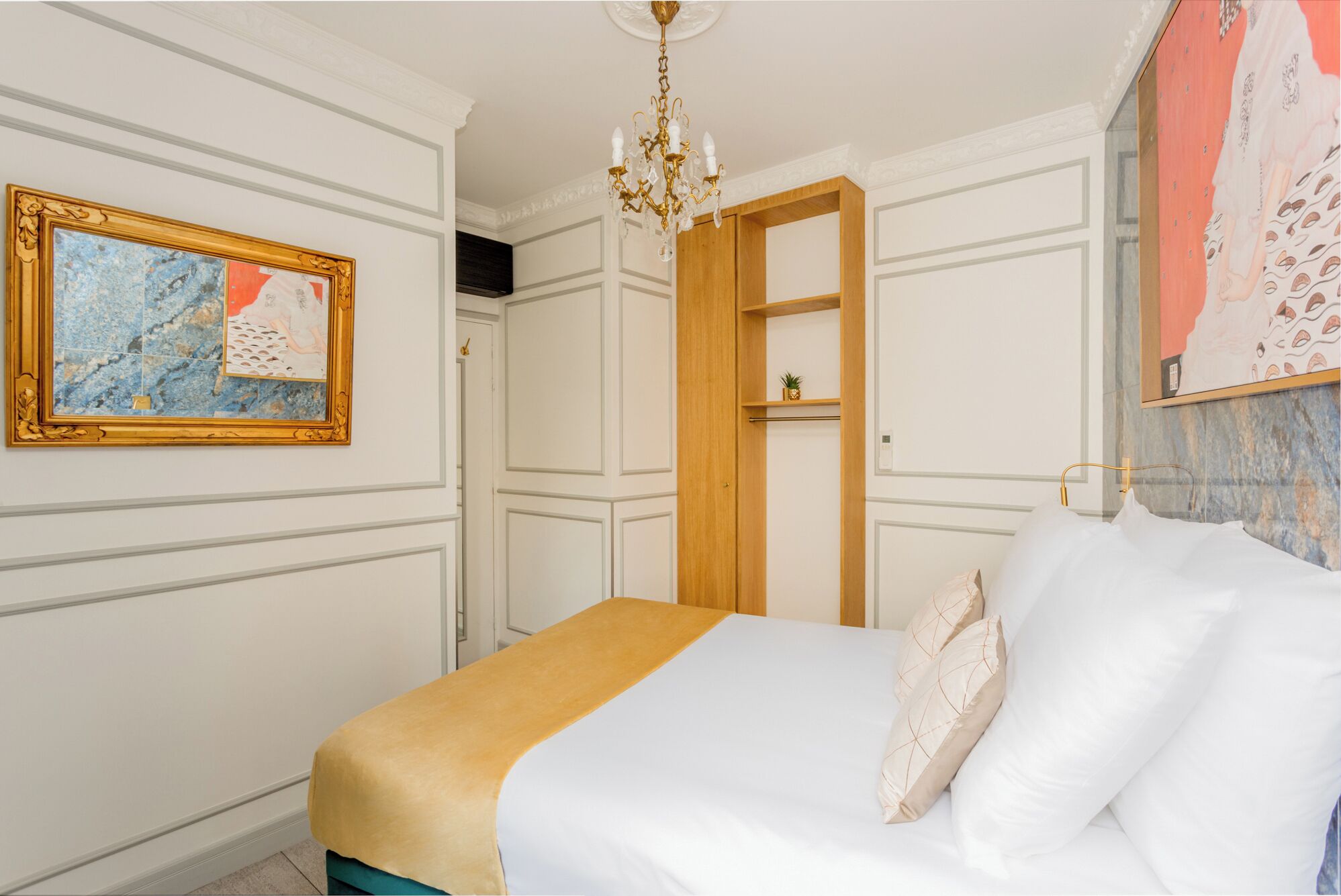 A bedroom with a bed, a chandelier, a wardrobe, and a painting on the wall.