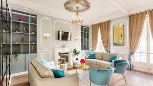 A living room with a sofa, chairs, a TV, a chandelier, and a bookshelf. - Merveil Luxury Suites - Septembre I-II (Paris)