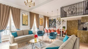 A spacious living room with a sofa, chairs, a coffee table, and a staircase leading to a kitchen. - Merveil Luxury Suites - Septembre I-II (Paris)