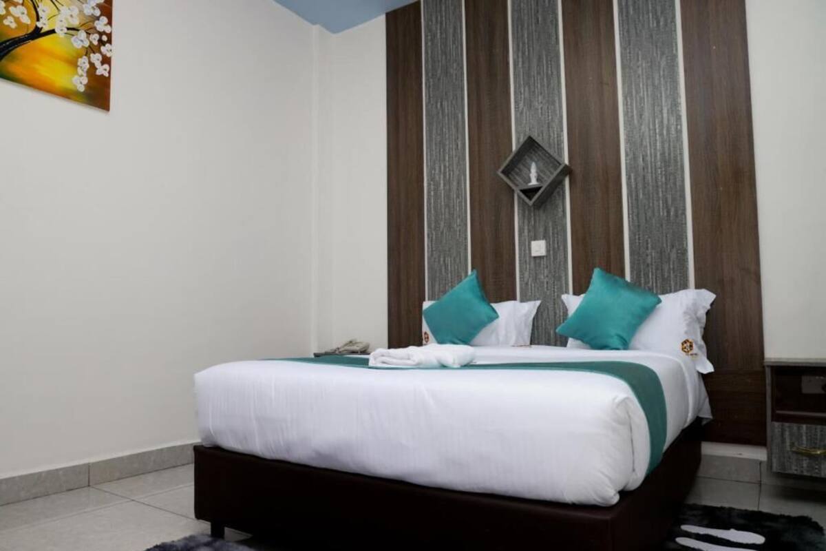 A neatly made bed with white and teal bedding, a dark wooden headboard, and a wall-mounted light fixture.