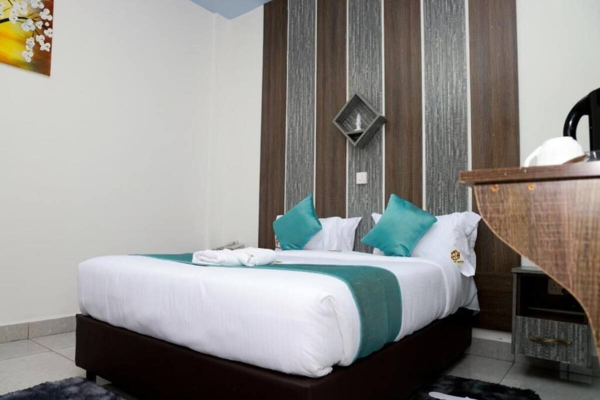 A neatly made bed with white and teal bedding, a wooden headboard, and a small bedside table with a lamp.