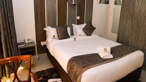 A neatly made bed with a white and brown bedspread, a decorative pillow, and a small bedside table with a phone. - The Gem Hotel Naivasha (Naivasha)