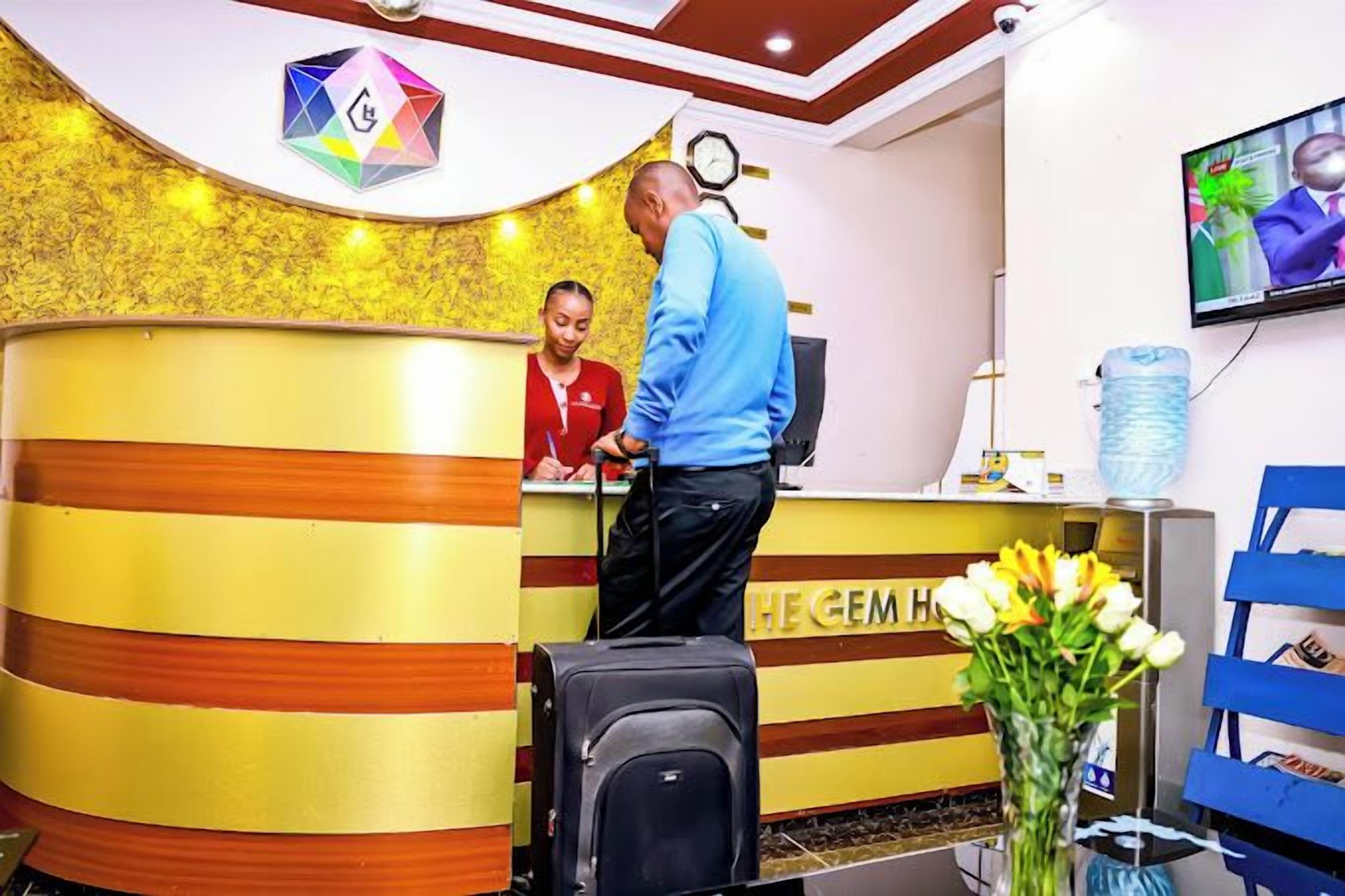 A reception desk with a receptionist, a man standing, and a TV screen.
