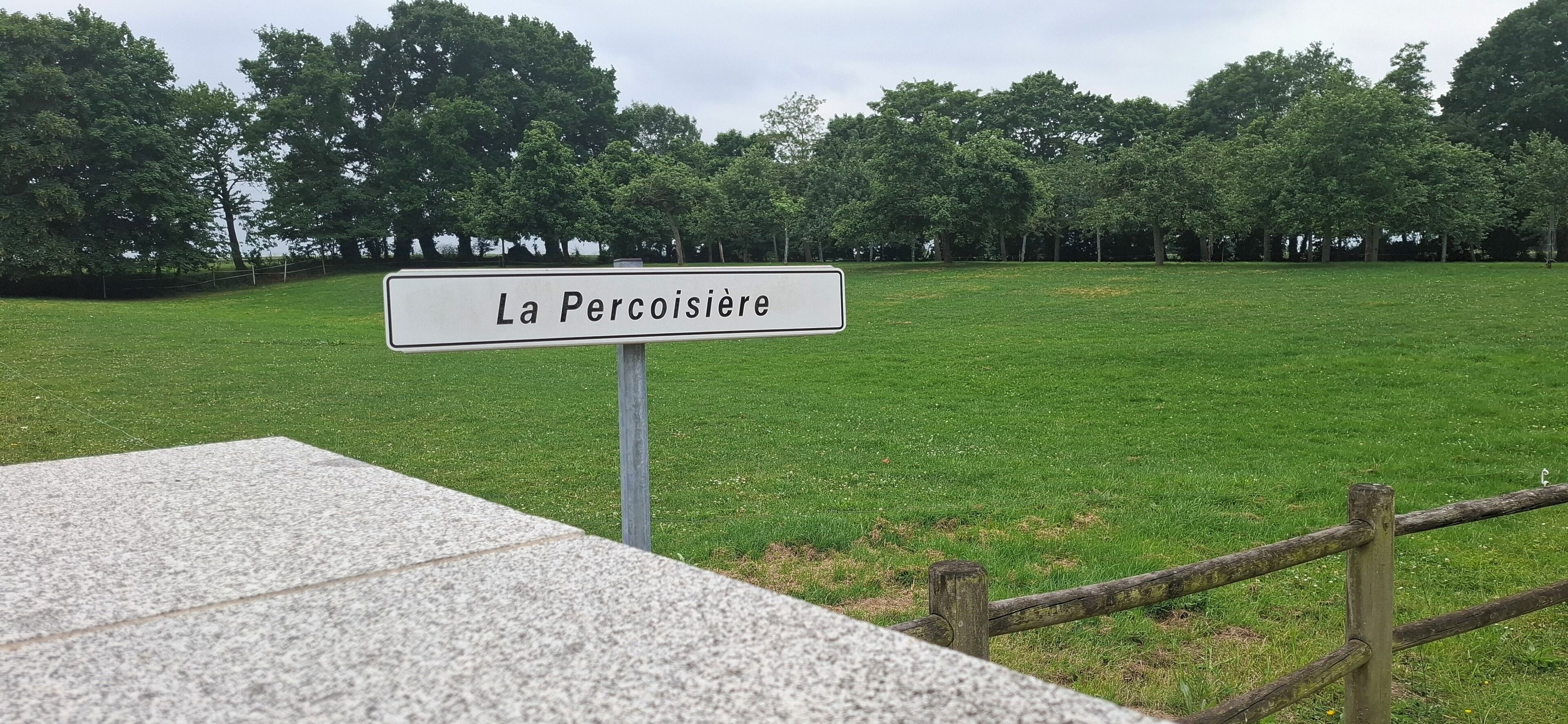 Un panneau indiquant « La Percoisière » dans un champ herbeux, avec des arbres en arrière-plan.