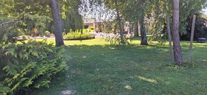 Un jardin bien entretenu, agrémenté de divers arbres et arbustes, d’une pelouse et d’un bâtiment visible au loin.