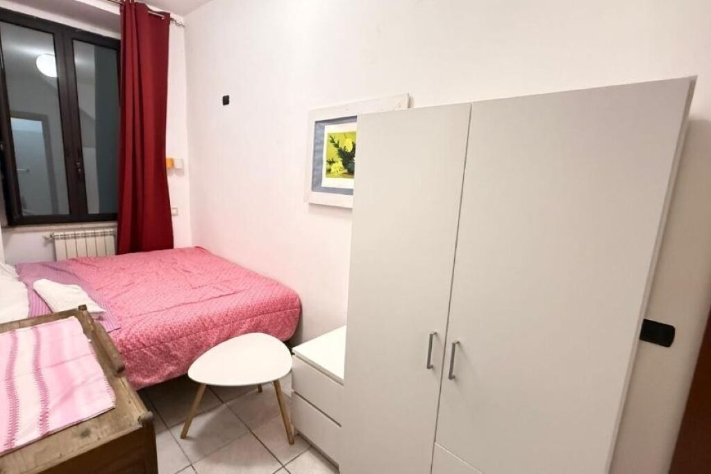 A bedroom with a bed, a white wardrobe, a small table, and a window with curtains.