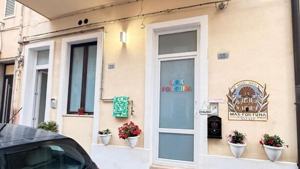 A building with a sign reading "MAX FORTUNA" and a logo for "GUEST HOUSE MAX FORTUNA". There are potted plants on the ground floor and a car parked in front. - Max- Fortuna ground floor apartment (Ragusa)