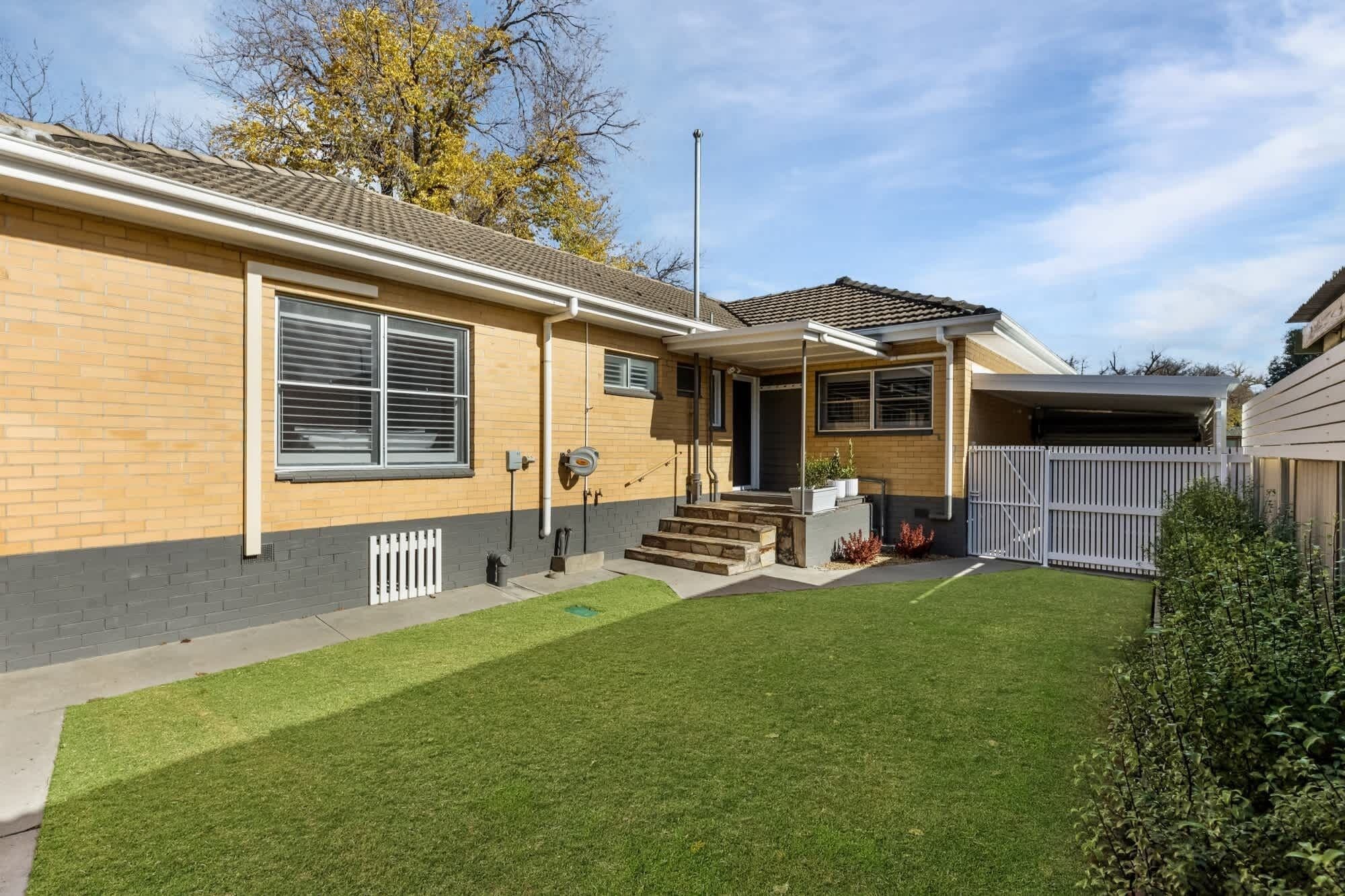 Ein zweistöckiges Haus mit Veranda, Garage und einem eingezäunten Garten.