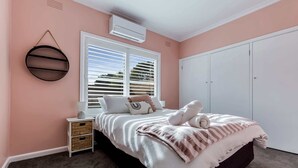 A bedroom with a bed, a nightstand, a wall-mounted air conditioner, and a window with blinds. - Kennington House, 3BR Home in Bendigo City (Kennington)