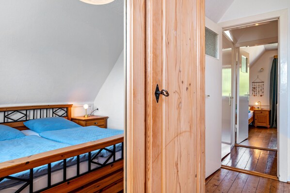 A bedroom with a wooden bed, a nightstand, and a door leading to a bathroom. - Holiday Home 'Svea' with Private Terrace, Private Garden and Wi-Fi (Cuxhaven)
