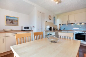 A kitchen with a dining table, chairs, a microwave, a coffee maker, and a clock on the wall.