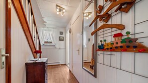 Een gang met houten vloer, een houten deur, een klein tafeltje met een vaas en een houten houten trein die aan de muur hangt.