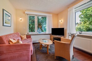 A living room with a sofa, a small table, a wicker chair, a television, and a window with curtains.