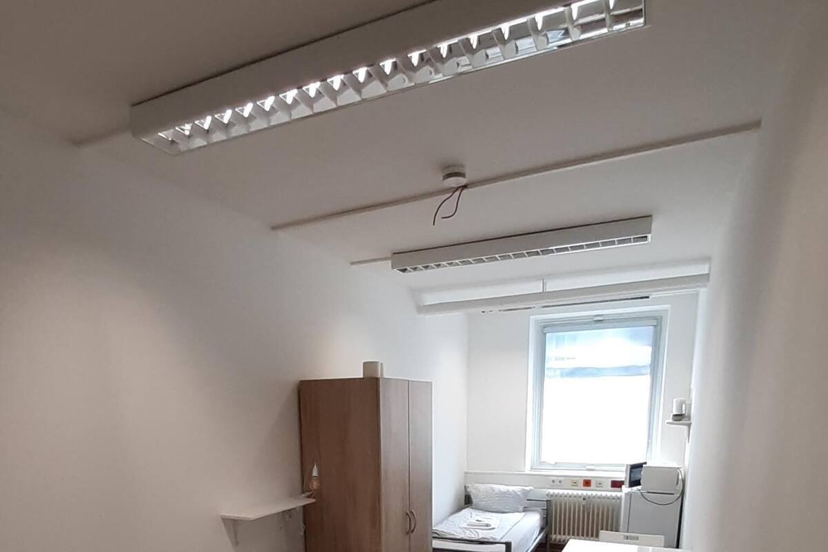 A compact room with a bed, a wardrobe, a small table, and a chair.