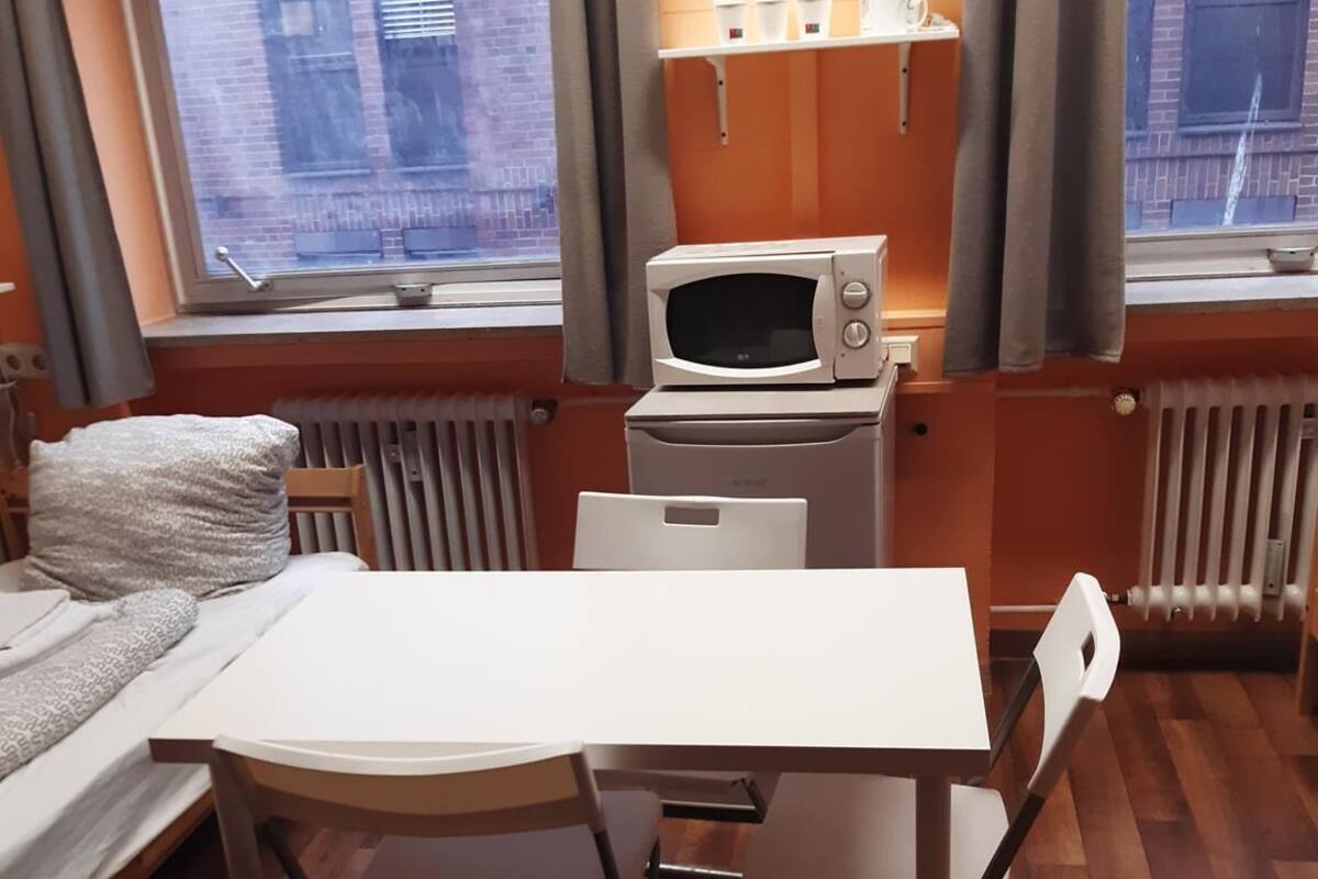 A compact room with a bed, a small table, and a microwave.