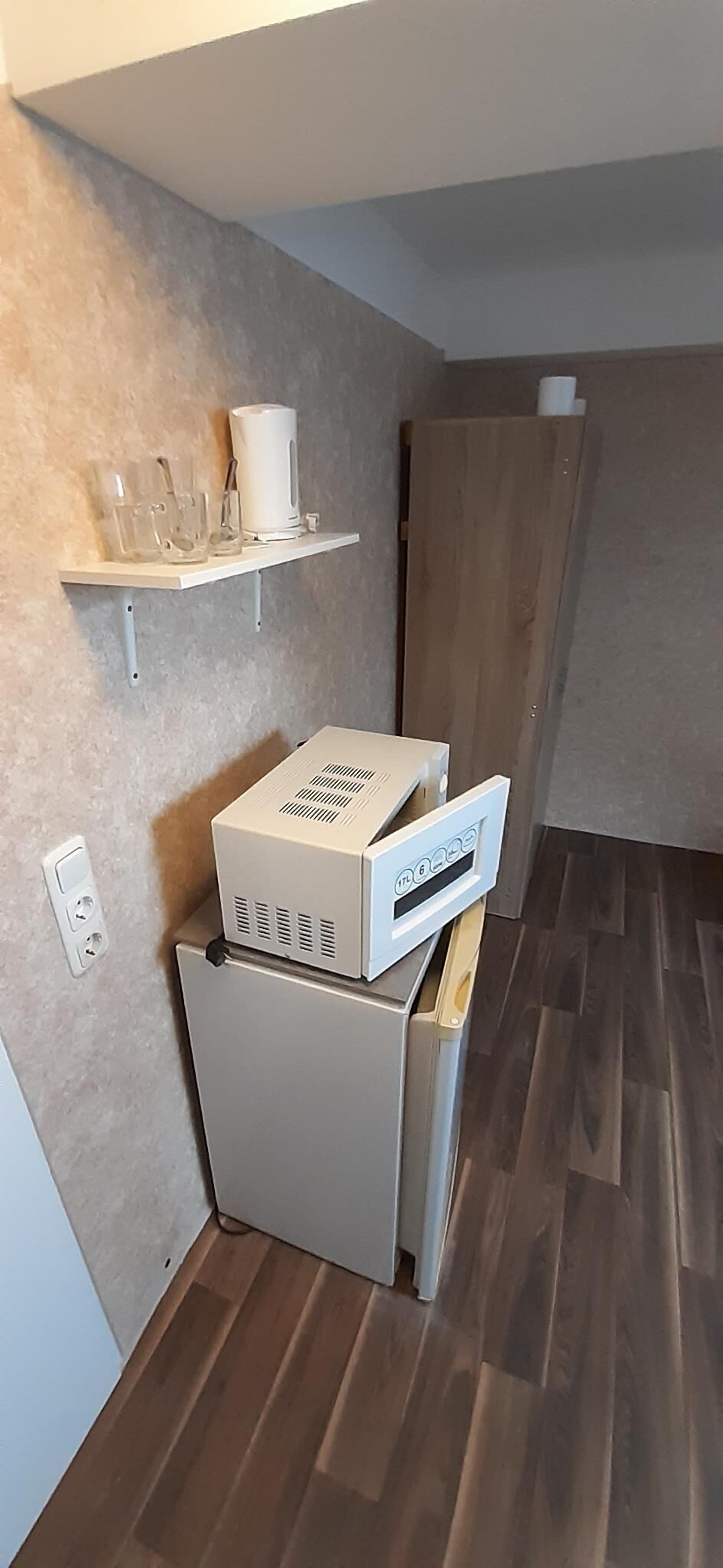 A compact kitchenette with a small refrigerator, a microwave, and a coffee maker on a white shelf.