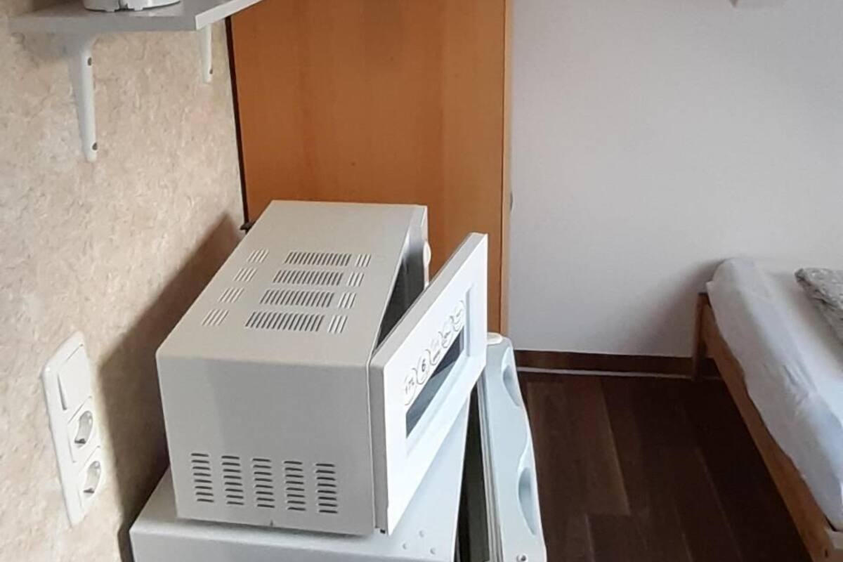 A compact room with a bed, a wooden wardrobe, and a small shelf with a kettle and glasses.