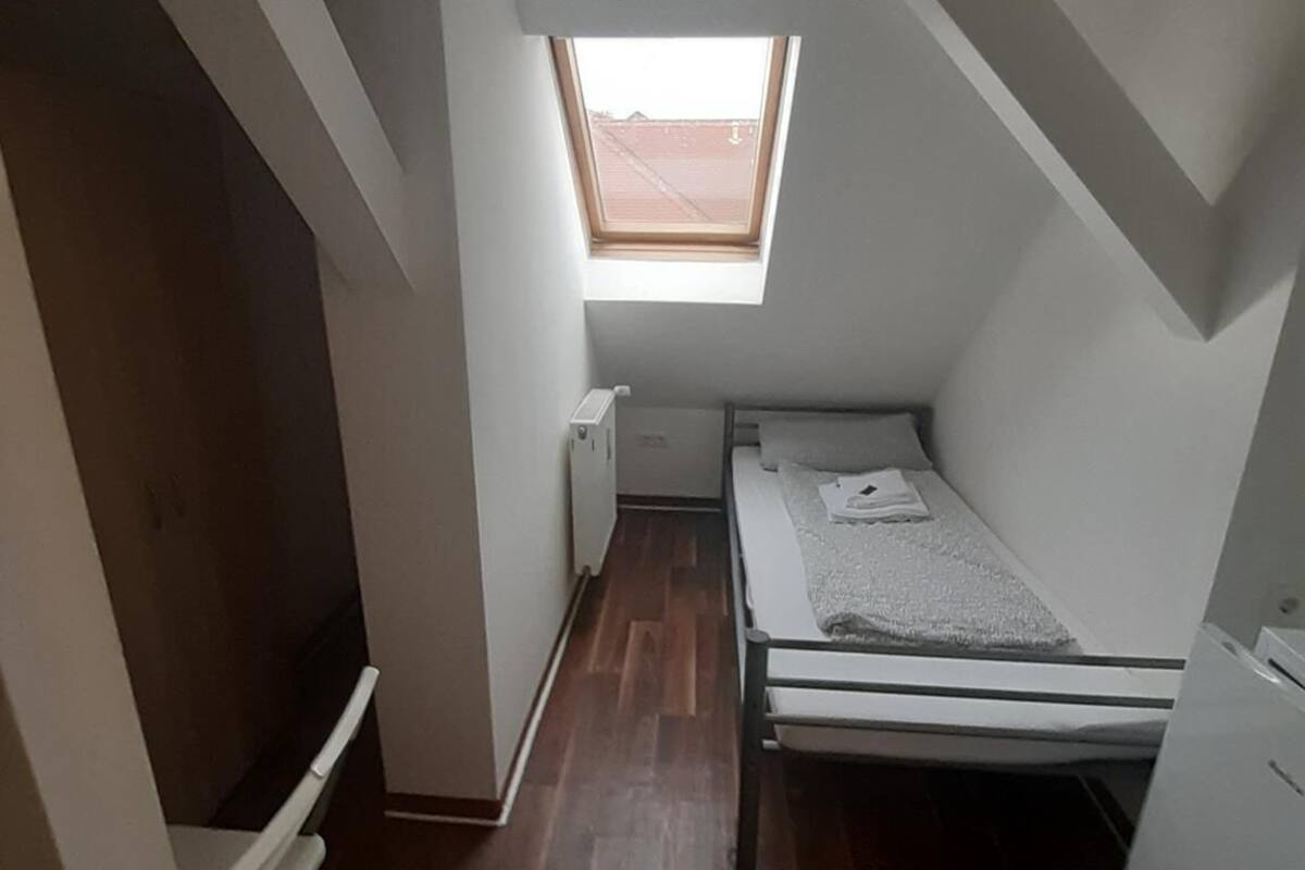 A small, narrow room with a sloped ceiling and a skylight. It features a single bed, a radiator, and a white wardrobe.