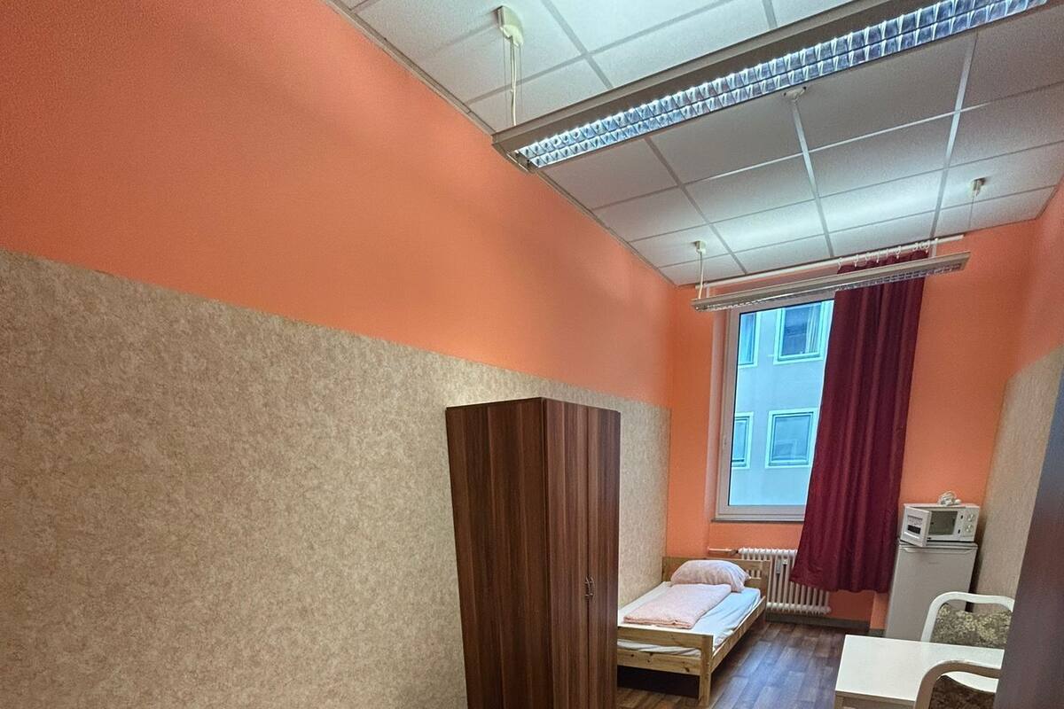 A room with two single beds, a wooden wardrobe, a small table, and a window with curtains.