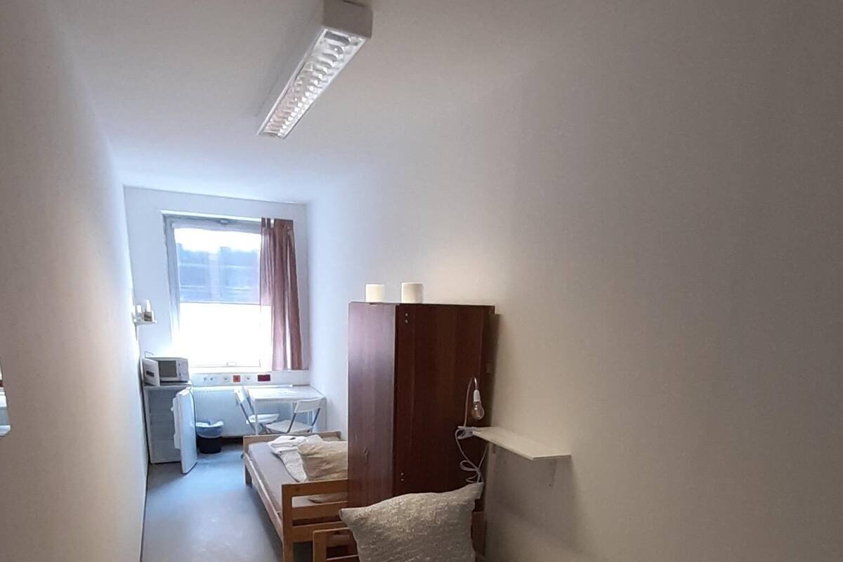 A narrow hallway with a bed, a wardrobe, and a desk with a chair.