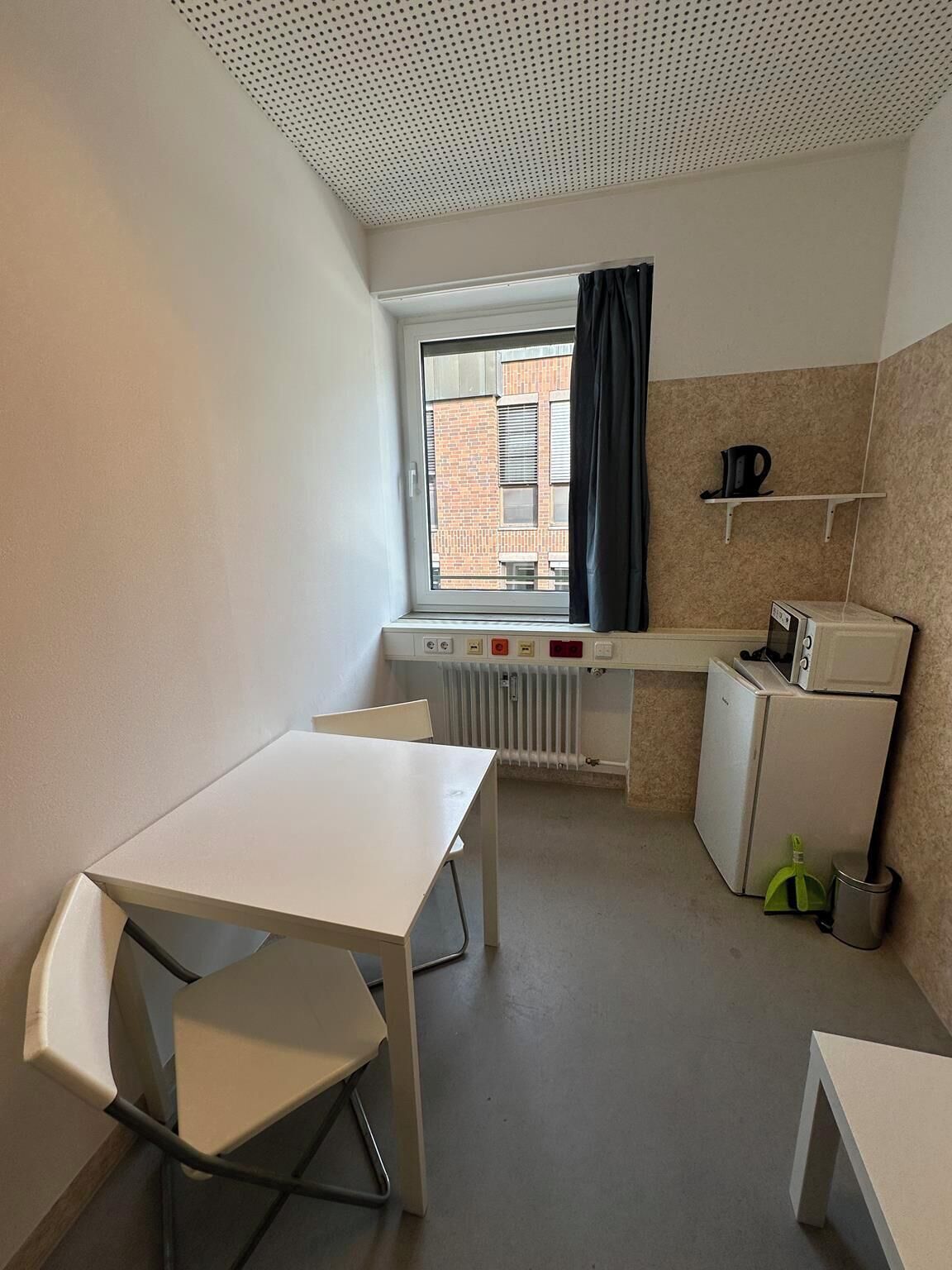 Eine kompakte Küchenzeile mit Fenster, Heizkörper, kleinem Kühlschrank und Tisch mit Stühlen.