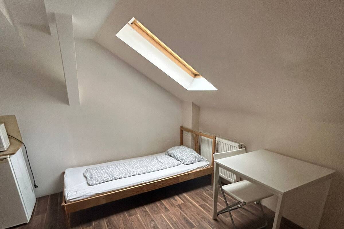 A compact room with a loft bed, a small desk, and a radiator.