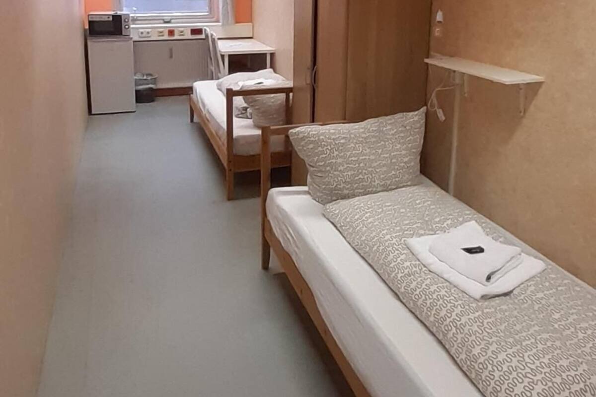 A compact hotel room with a single bed, a small desk with a chair, a wardrobe, and a window with curtains.