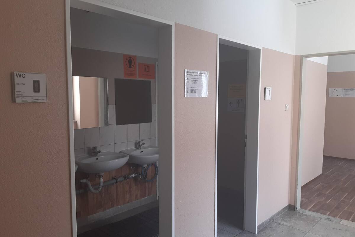 A restroom with two sinks, a mirror, and a sign indicating the location of the toilet and shower.