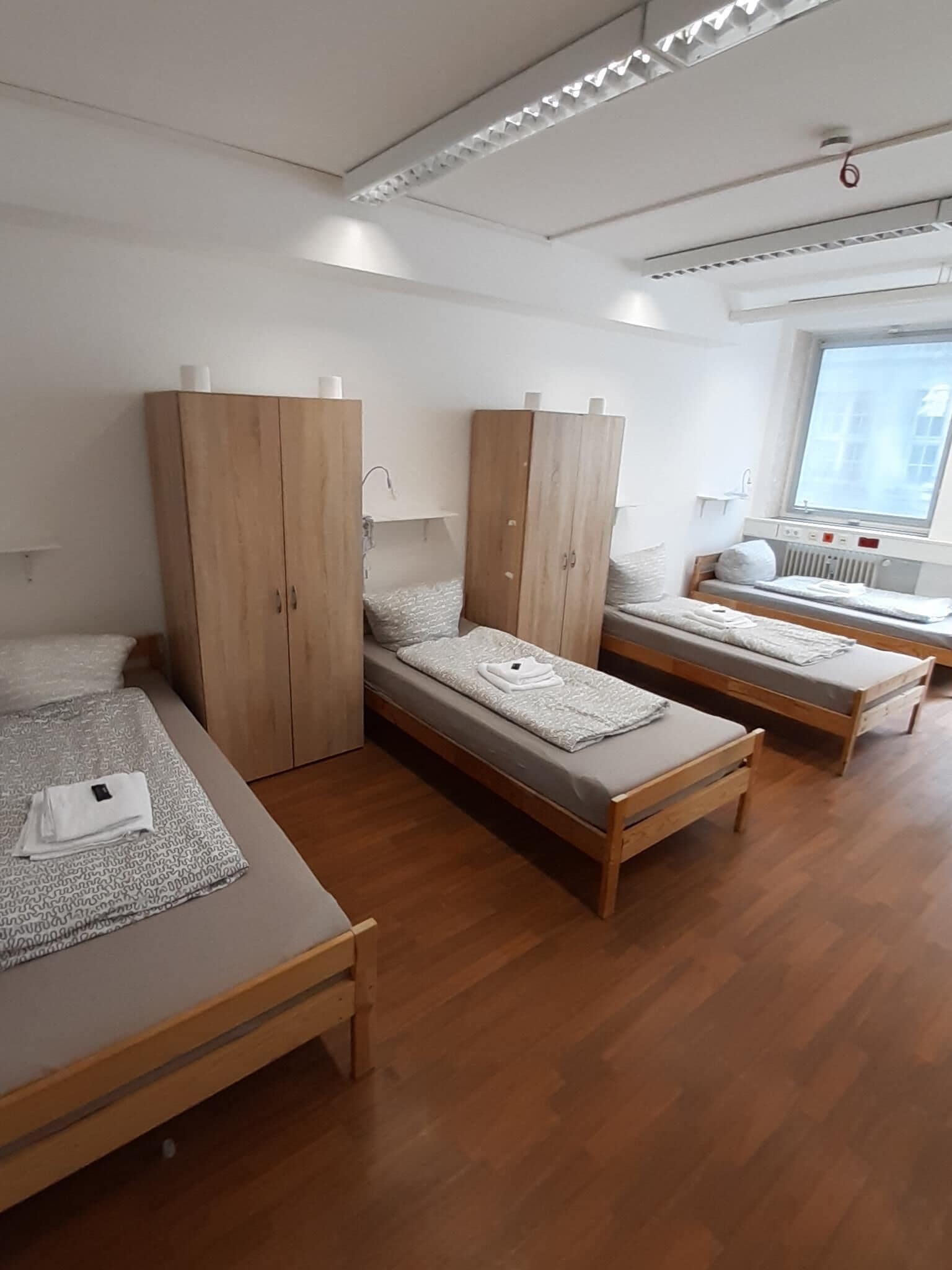 Een hotelkamer met drie houten bedden, een grote kast, een raam met uitzicht en een radiator.