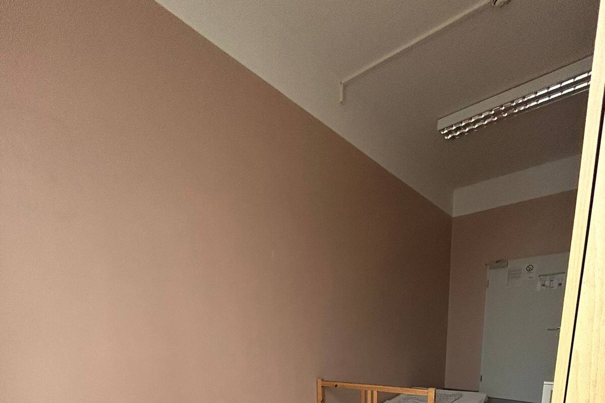 A dormitory room with two single beds, a wooden desk, and a wardrobe.