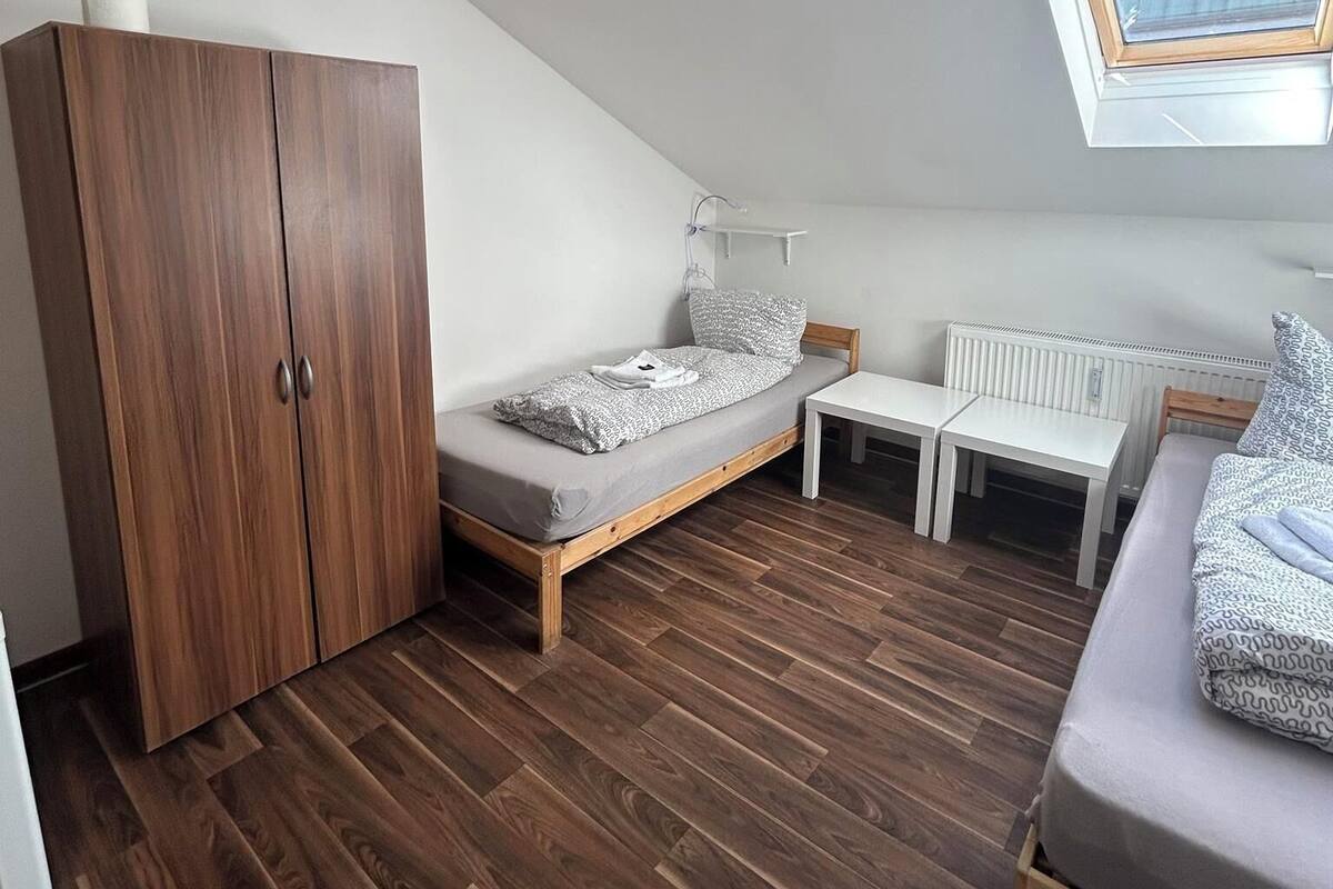 A small, well-lit attic bedroom with a sloped ceiling, a skylight, a wardrobe, a bed, a desk, and a radiator.