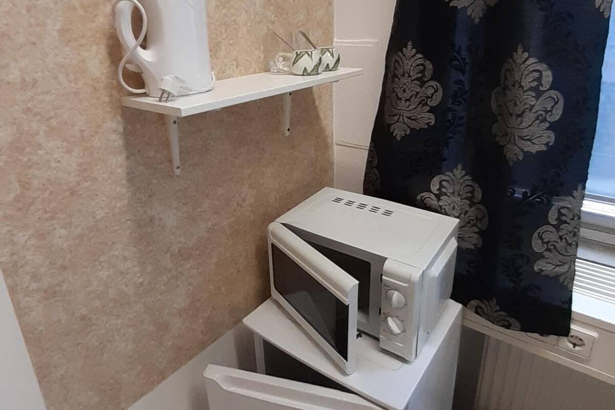 A compact kitchenette with a microwave, a small refrigerator, and a shelf holding a coffee maker and a glass.
