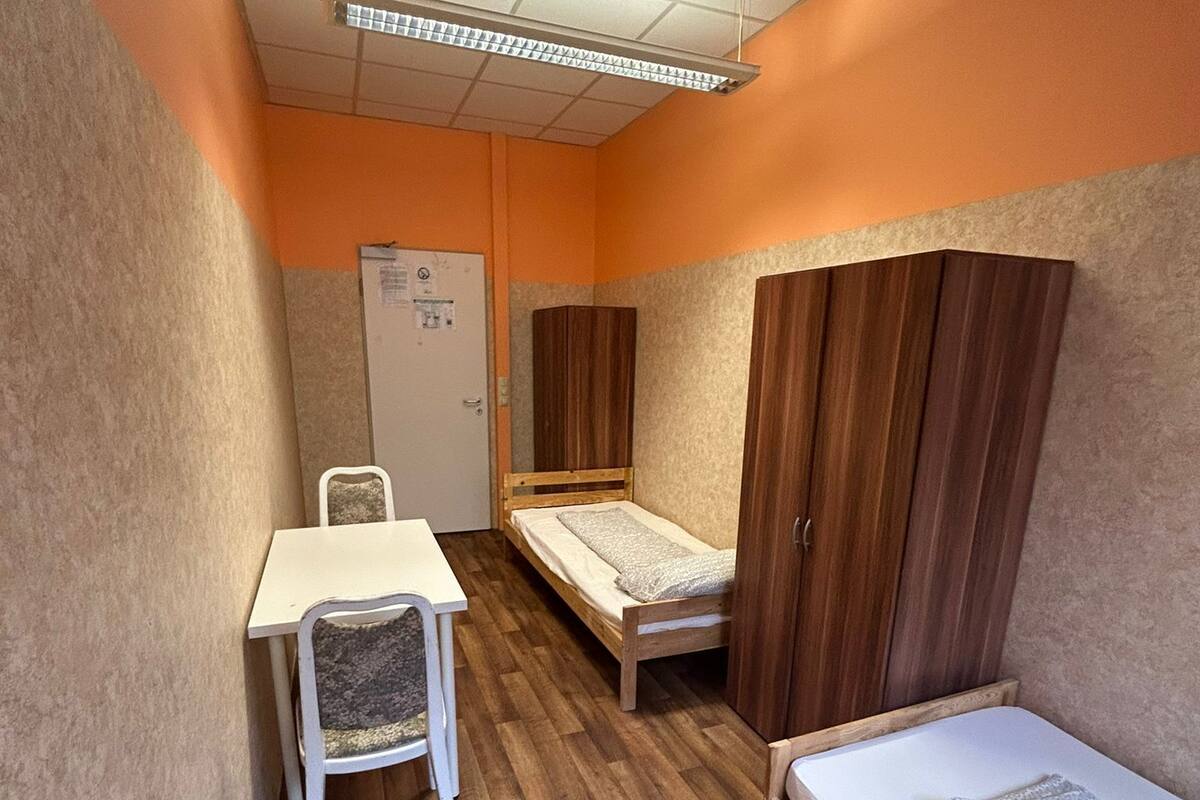 A dormitory room with two single beds, a desk, a chair, and a wardrobe.