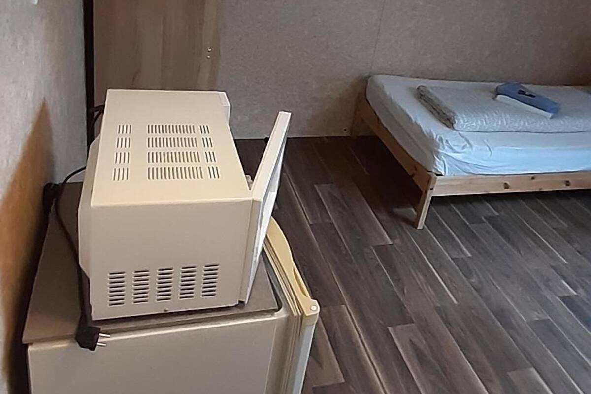 A compact room with a small bed, a desk with a computer, and a shelf with glasses and a candle.