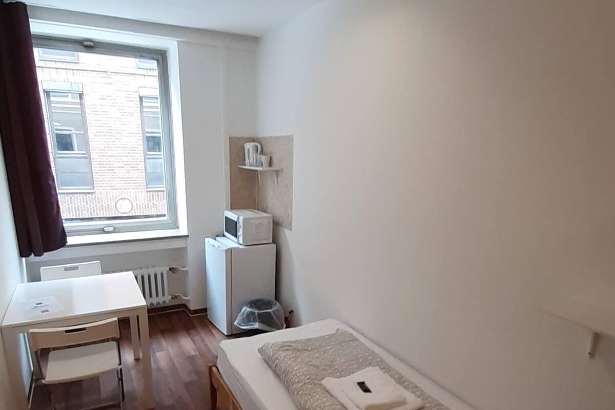 A small, clean room with a single bed, a desk, and a window.