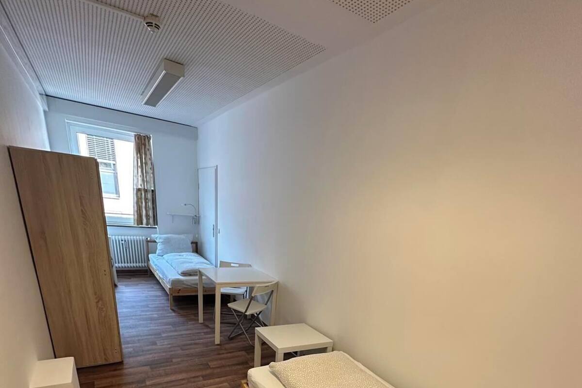 A modern, minimalist room with a wooden floor, a single bed, a small table, and a chair.