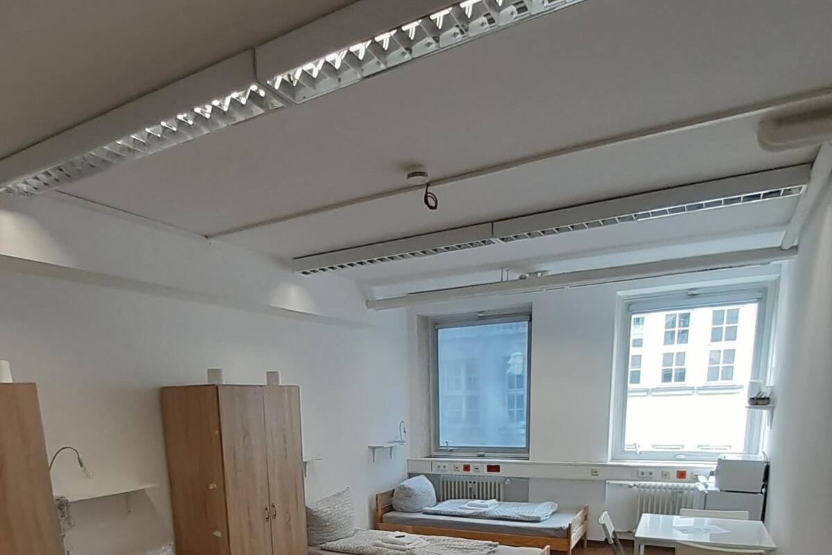 A modern, well-lit room with two wooden beds, a small desk, and a window providing natural light.