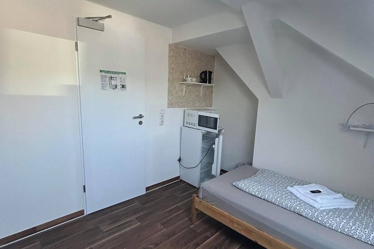 A compact room with a bed, a microwave, and a small kitchenette.