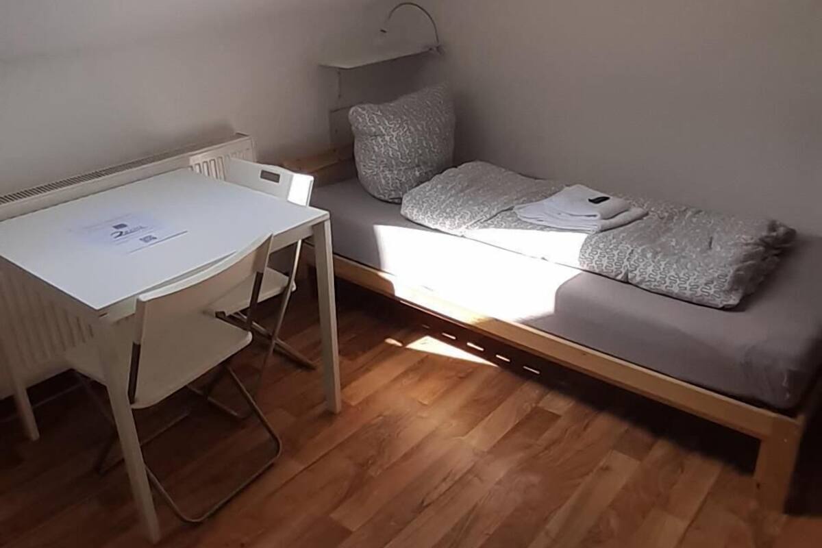 A small room with a slanted ceiling, a desk with papers, a bed with pillows, and a skylight.