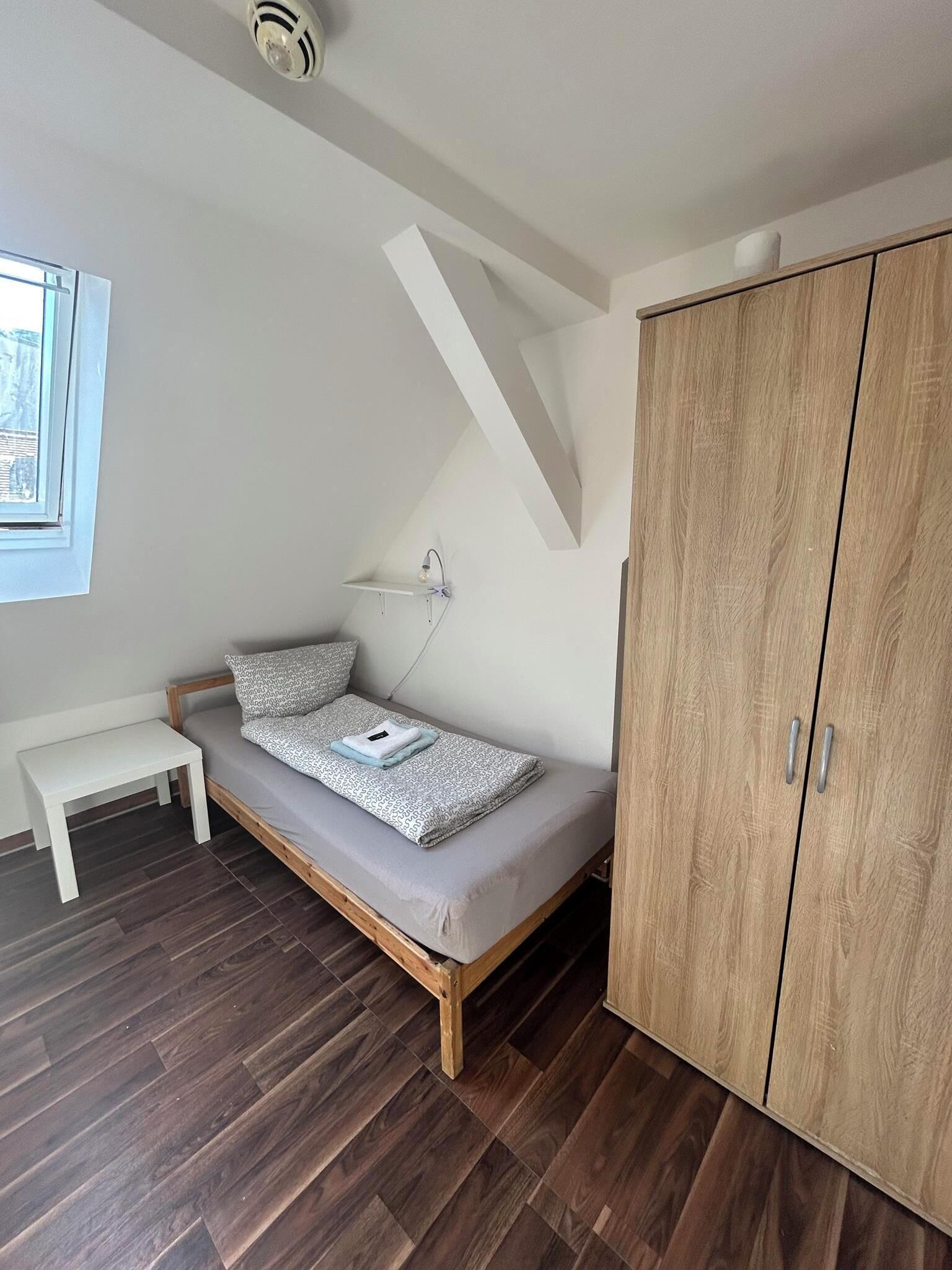 Une petite pièce moderne avec un lit en mezzanine, une armoire en bois, un petit banc et une fenêtre.