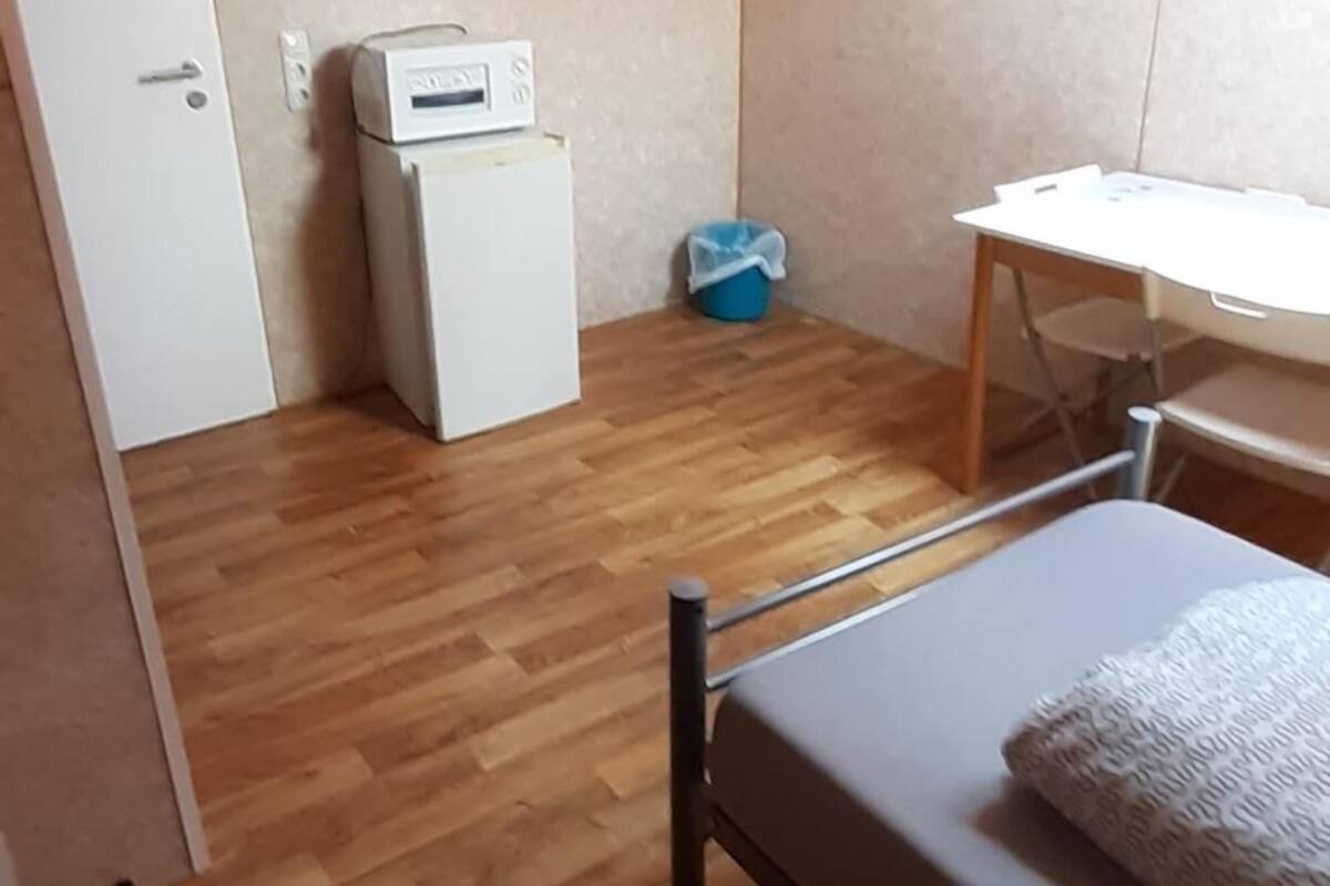 A small, compact room with a bed, a desk, and a kitchenette area.