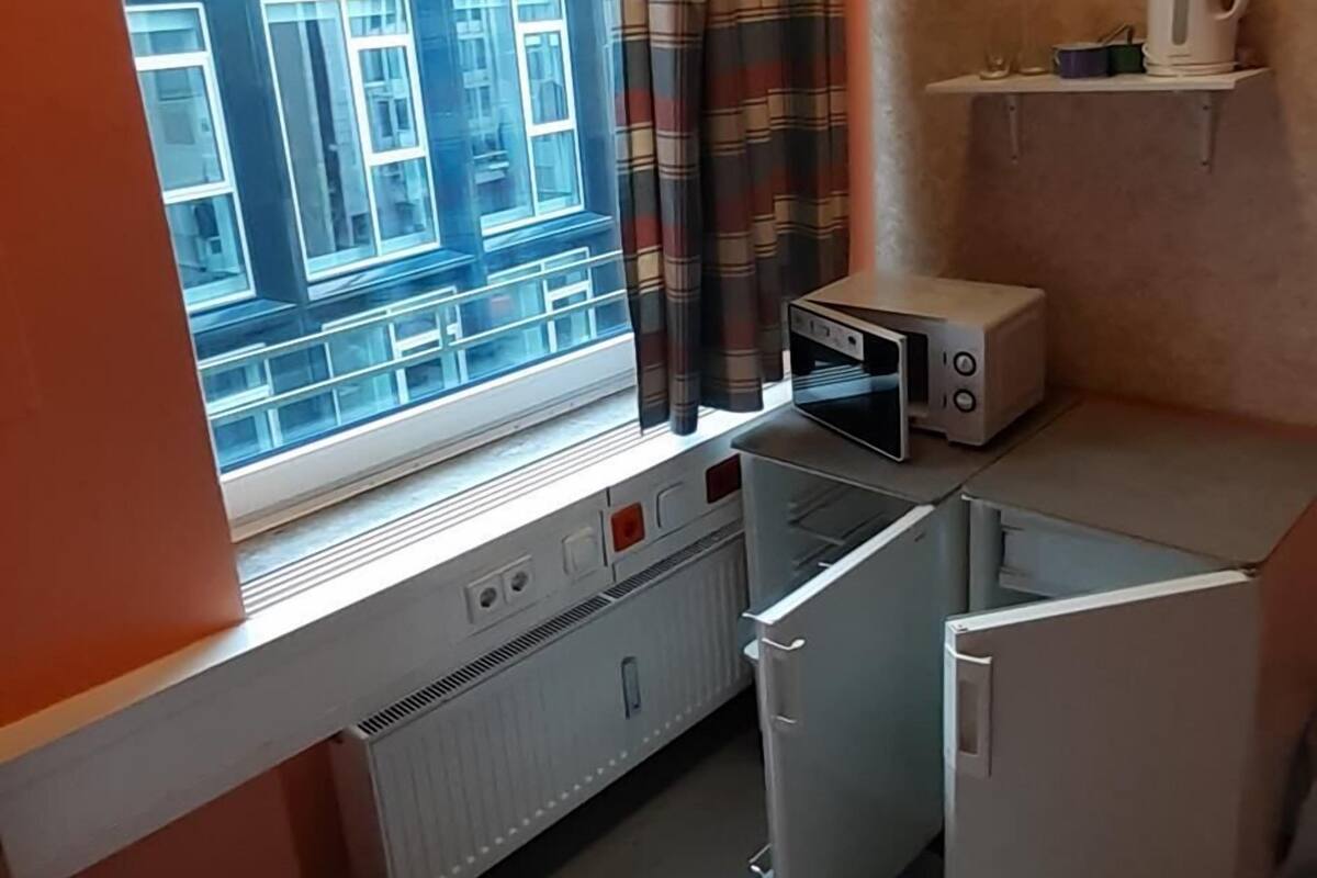 A compact kitchen with a window, a microwave, a kettle, and a small shelf.