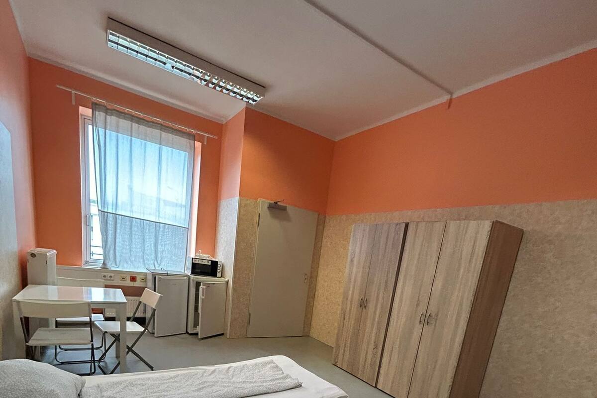 A bedroom with a bed, a desk, a chair, a wardrobe, and a window with curtains.