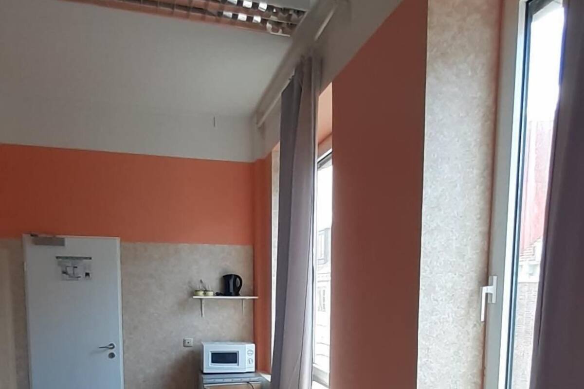 A compact room with a kitchenette, a dining table with chairs, a bed, and a window with curtains.