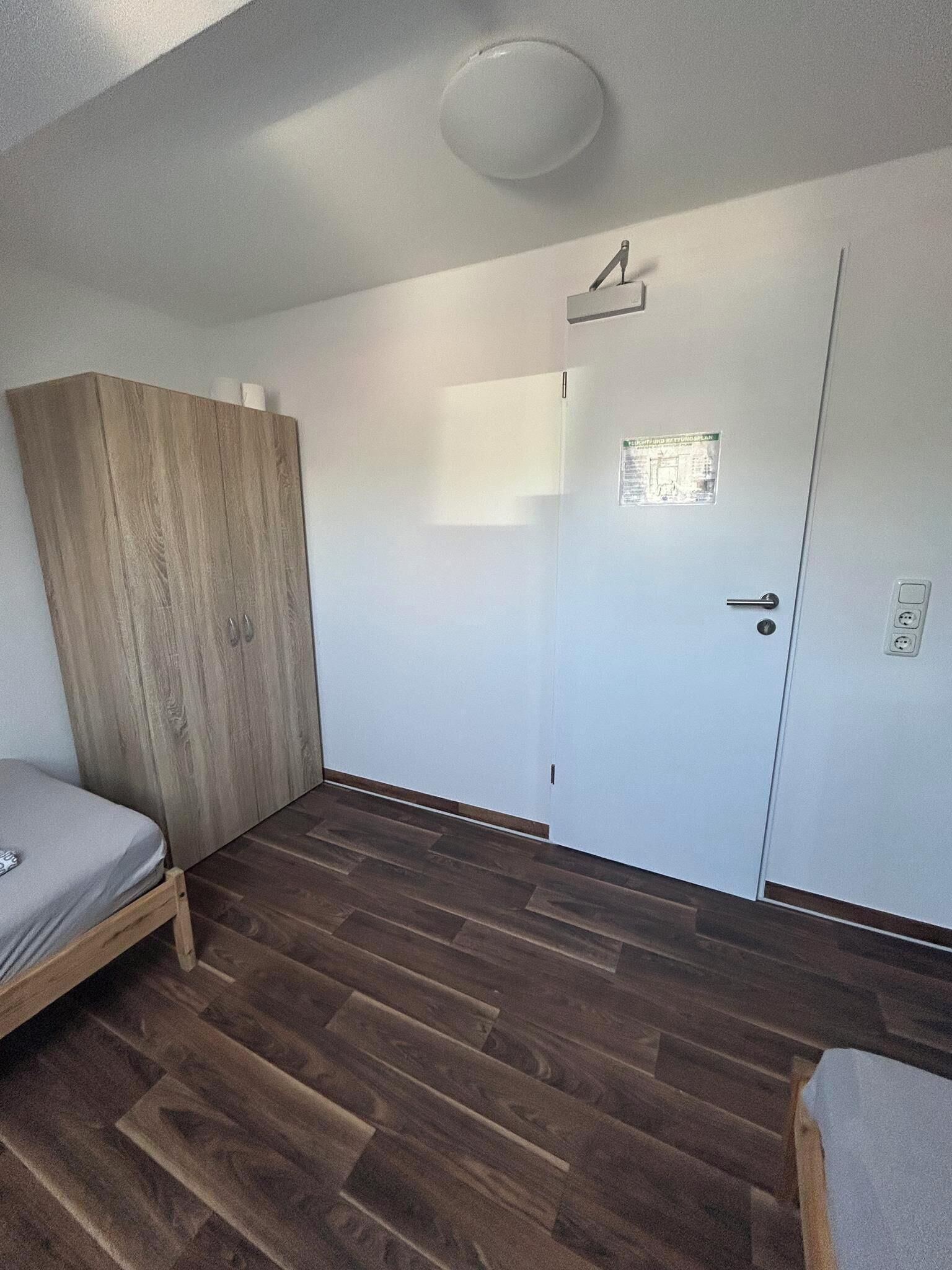 Un dormitorio con un armario de madera, una cama y una puerta blanca con un pequeño ventanal.